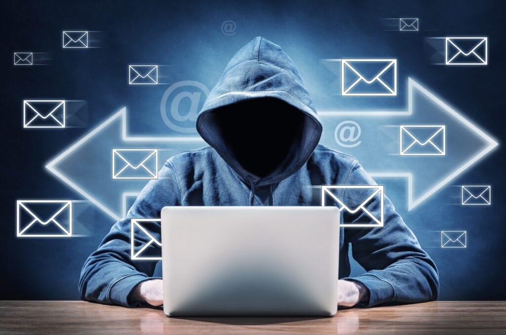 Man in hoodie with no face sending emails from a computer. Email icons flying around him. 